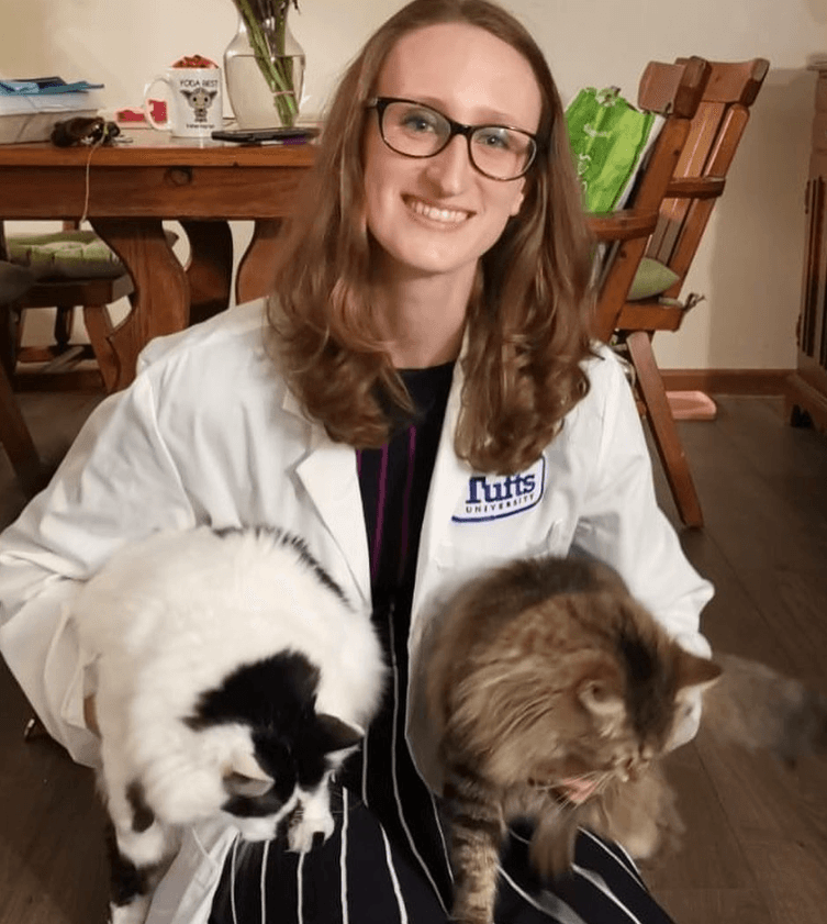 Sara in a Tufts white coat holding two cats.
